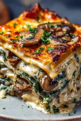 Creamy spinach mushroom lasagna served on a plate with fresh herbs
