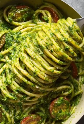 Plate of spinach pesto pasta garnished with pine nuts and cherry tomatoes