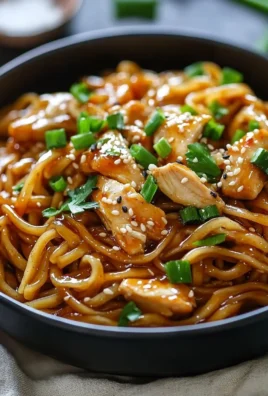 Plate of sticky garlic chicken noodles garnished with green onions