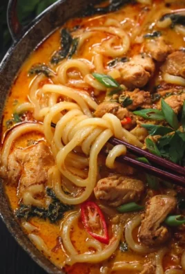 Bowl of Thai-inspired coconut red curry chicken udon with fresh herbs and vegetables.