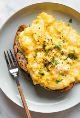 Plate of creamy cheesy scrambled eggs garnished with herbs