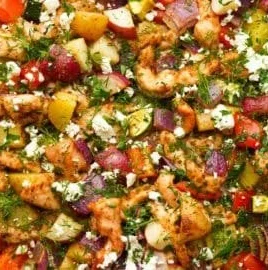Greek sheet pan chicken with colorful veggies on a baking tray