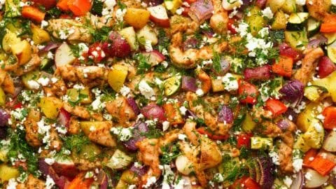 Greek sheet pan chicken with colorful veggies on a baking tray