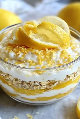 Bowl of lemon cheesecake overnight oats topped with fresh lemons and graham cracker crumbs.