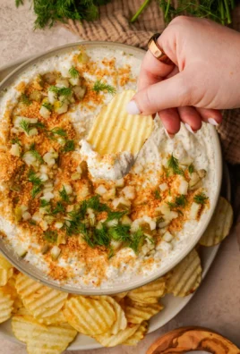 Creamy fried pickle dip served in a bowl with chips and pickles on the side.